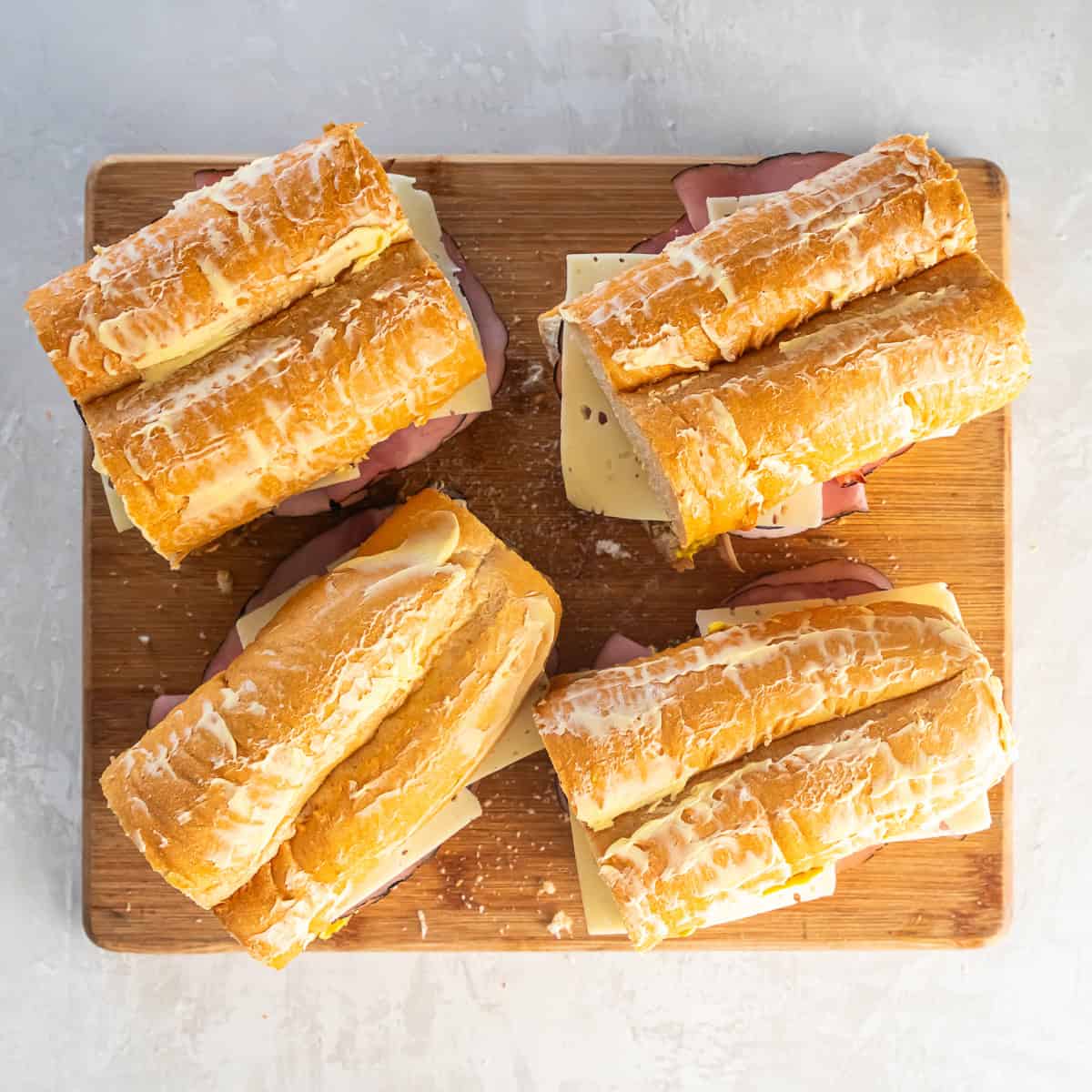Four assembed uncooked Cuban sandwiches on a board.