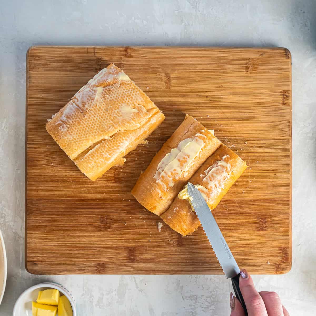 Softened butter being spread on the outside of Cuban bread before assembling Cuban sandwiches.