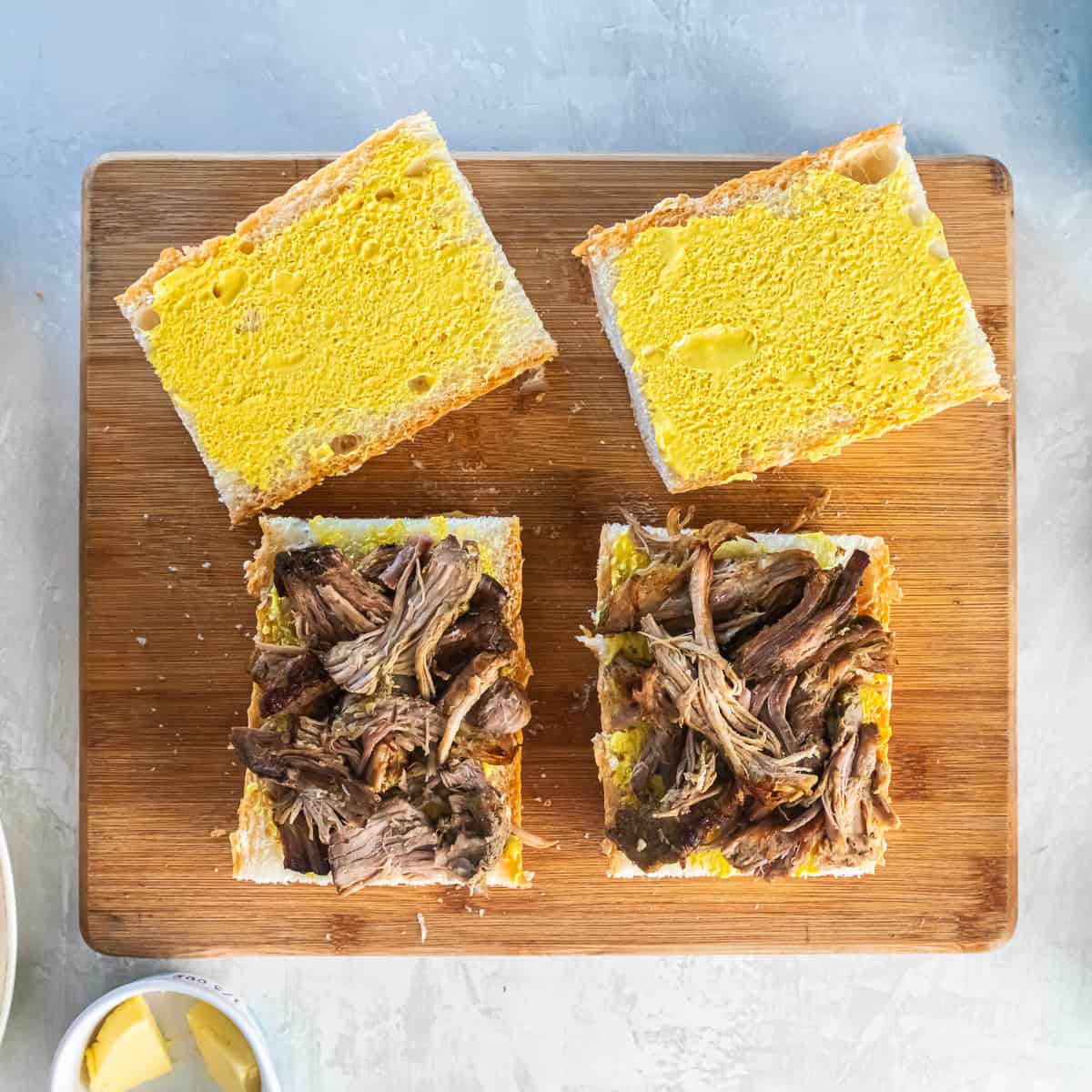 Shredded Cuban pork layered onto mustard-spread Cuban bread for Cuban sandwiches.