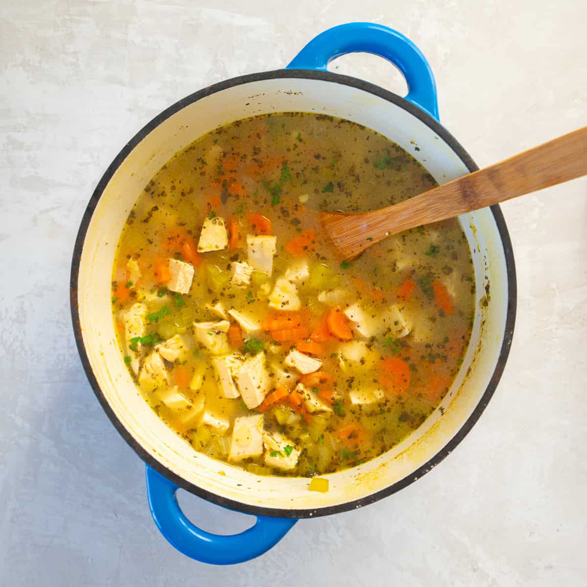 Pot of chicken soup simmering with chopped carrots, celery, onion, and chunks of chicken in a golden broth.