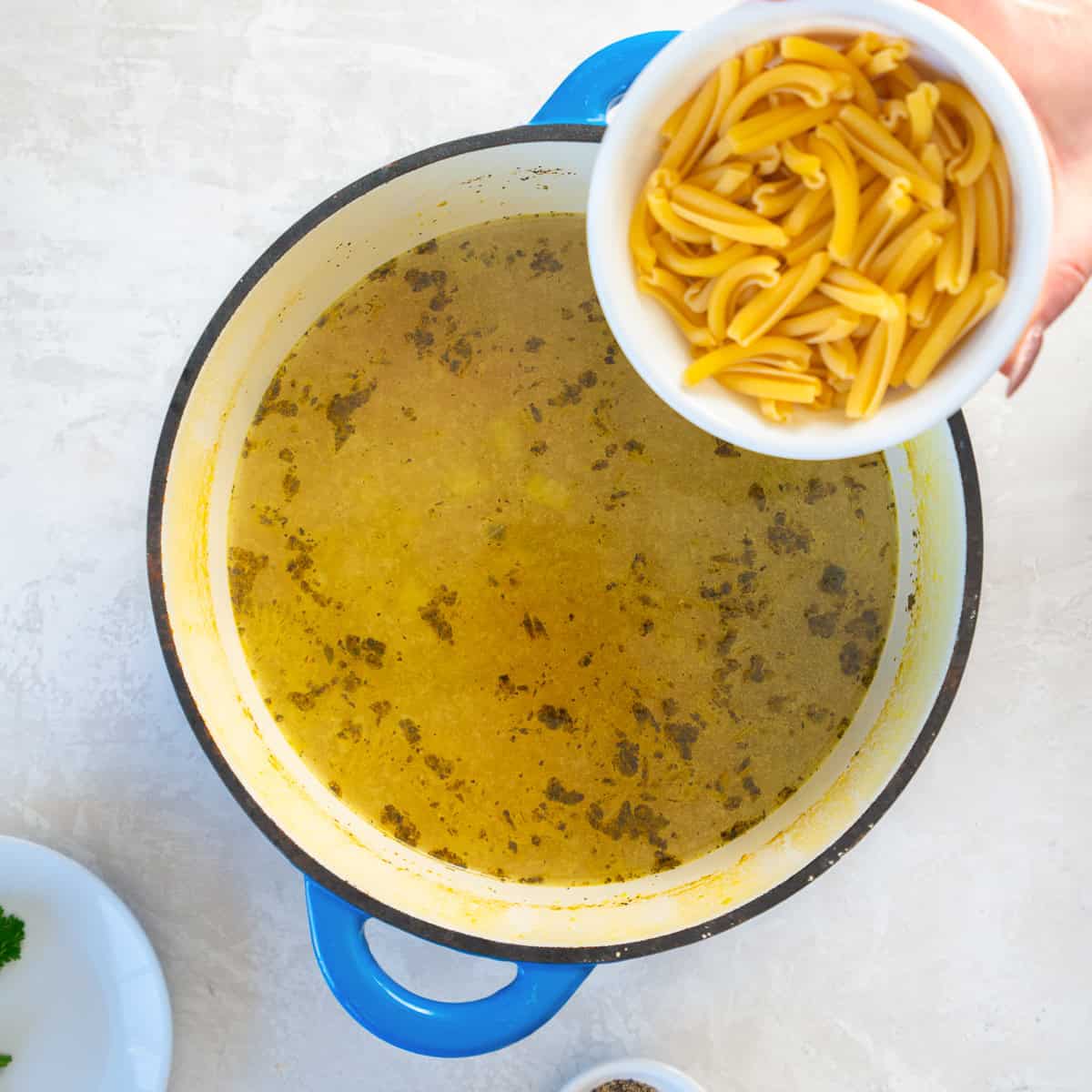 Uncooked short pasta being added to a pot of seasoned chicken broth.