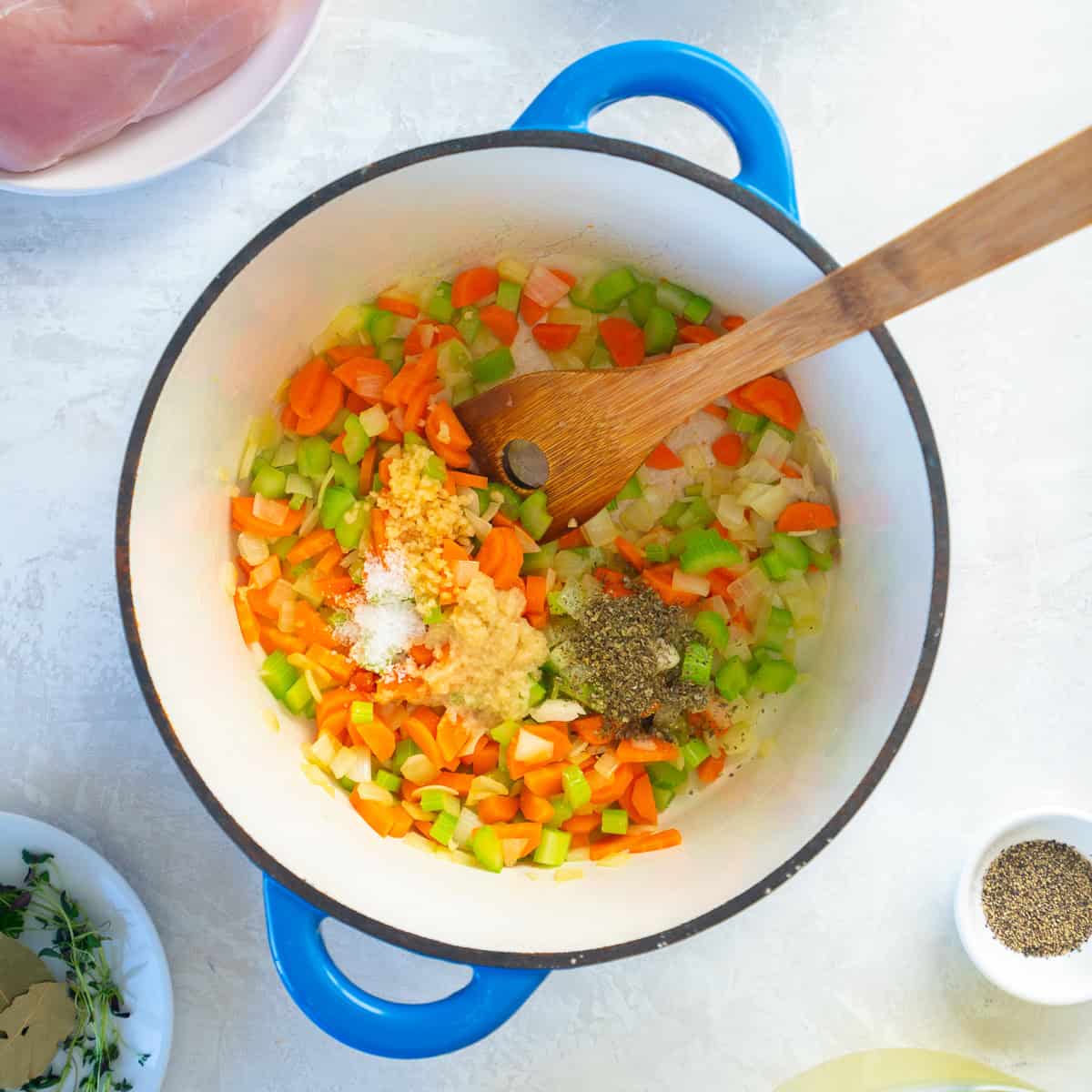 Chopped carrots, celery, and onion cooking in a pot with garlic, ginger, salt, pepper, and herbs.