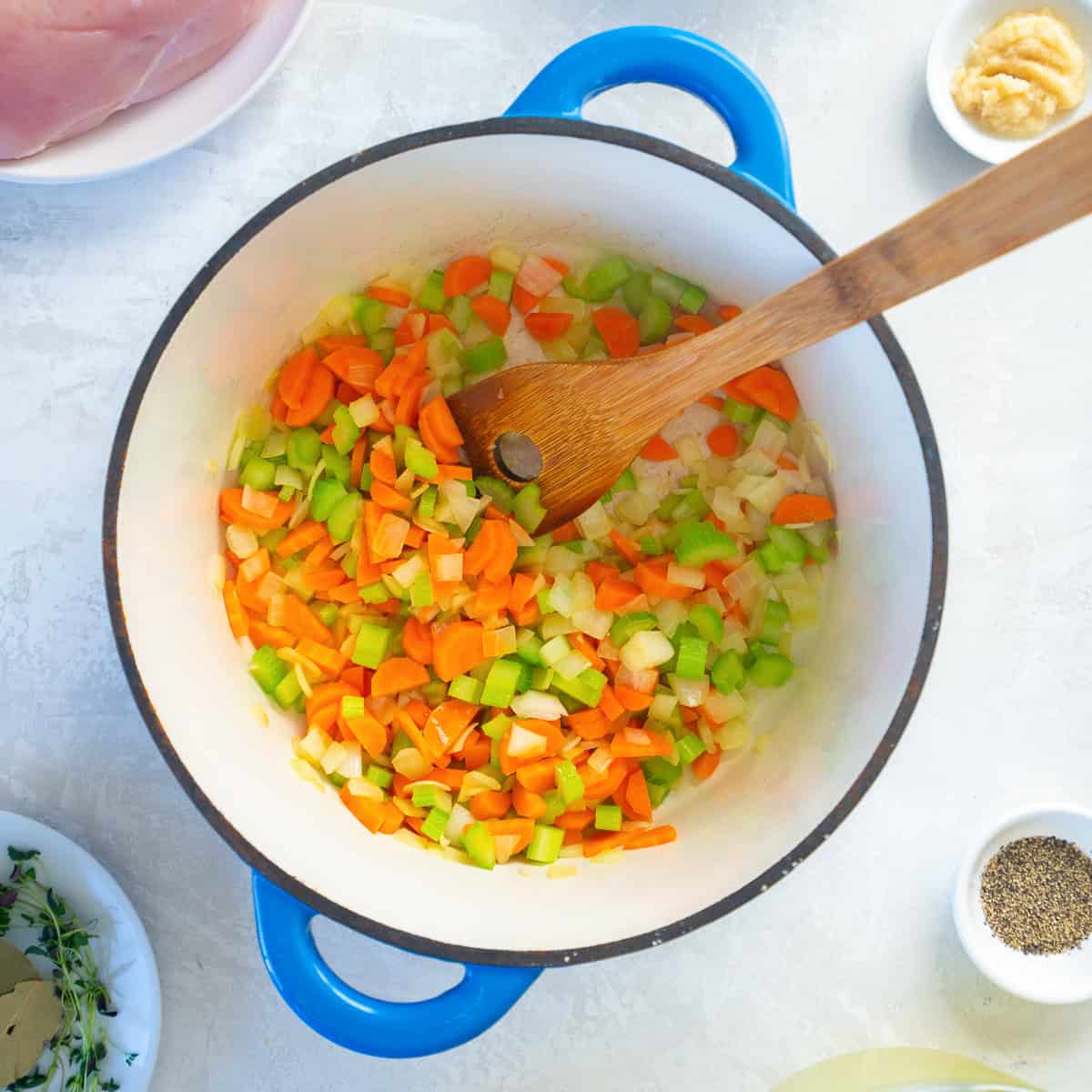 Chopped carrots, celery, and onion cooking in a pot with garlic, ginger, salt, pepper, and herbs.