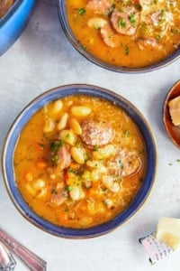 Bowl of sausage and bean soup with white beans, sliced sausage, carrots, celery, and a hearty, savory broth.