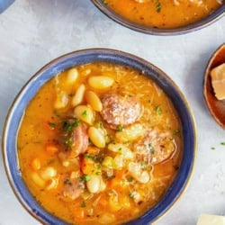 Bowl of sausage and bean soup with white beans, sliced sausage, carrots, celery, and a hearty, savory broth.