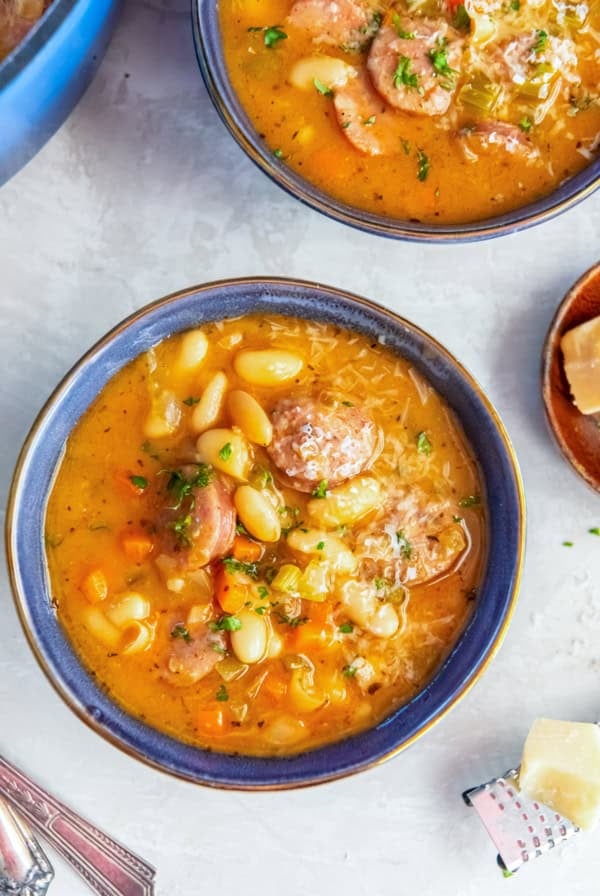 Bowl of sausage and bean soup with white beans, sliced sausage, carrots, celery, and a hearty, savory broth.