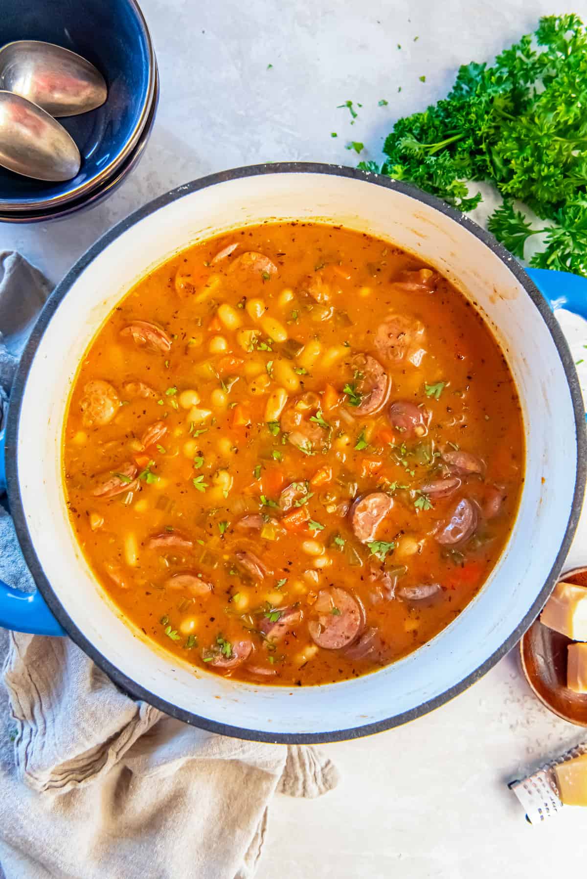 Dutch oven filled with hearty sausage and bean soup made with white beans, sliced sausage, carrots, and celery in a savory broth.