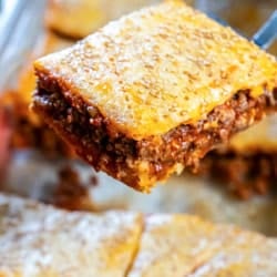 Sloppy Joe square being lifted from the pan, showing a golden, sesame-seed topped crescent roll crust and a thick, saucy beef filling.
