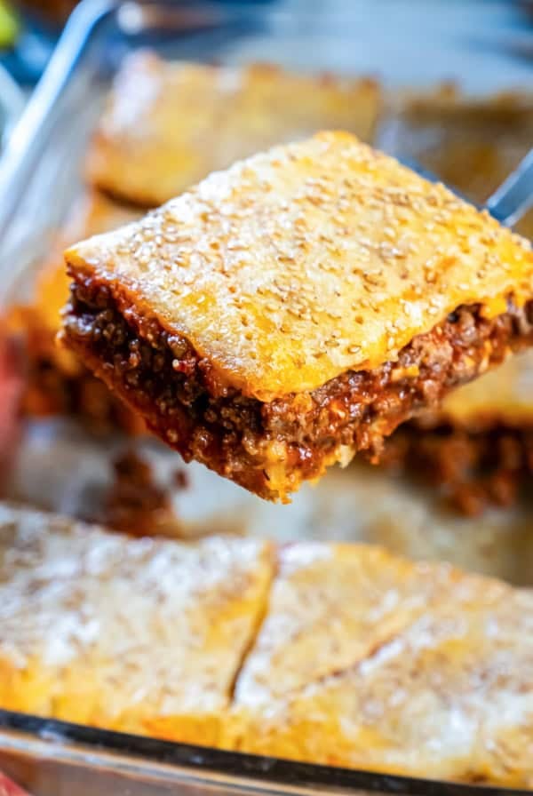 Sloppy Joe square being lifted from the pan, showing a golden, sesame-seed topped crescent roll crust and a thick, saucy beef filling.