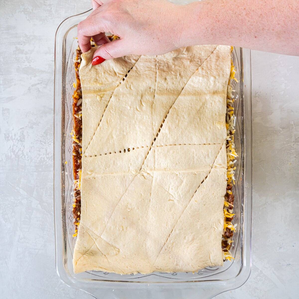 Second sheet of crescent roll dough being placed over the filling and cheese to form the top crust.