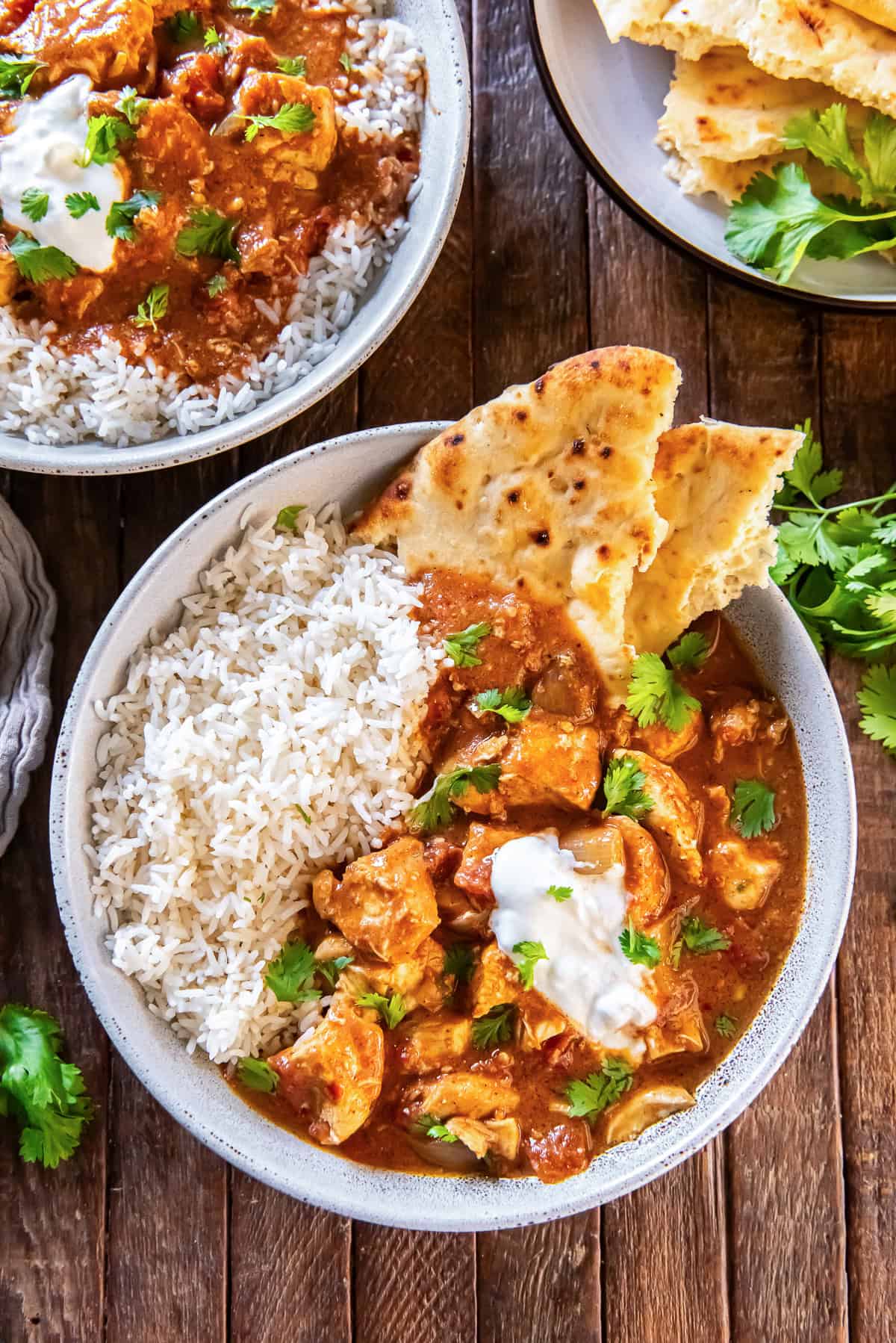 Overhead view of chicken tikka masala served over basmati rice with warm naan bread, garnished with fresh cilantro and a dollop of yogurt on a rustic wooden surface.