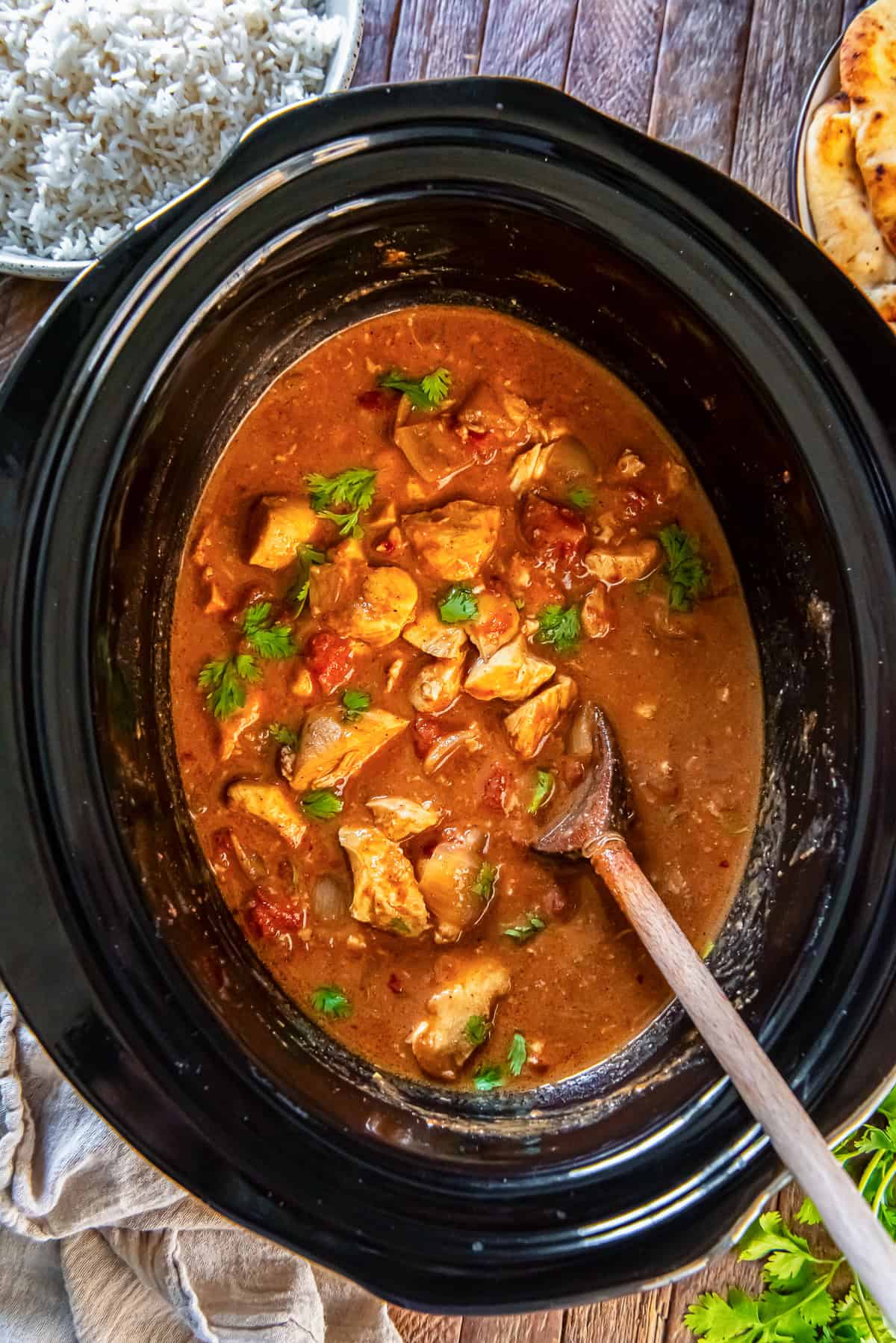 creamy chicken tikka masala in a slow cooker, garnished with fresh cilantro and a wooden spoon resting in the sauce.