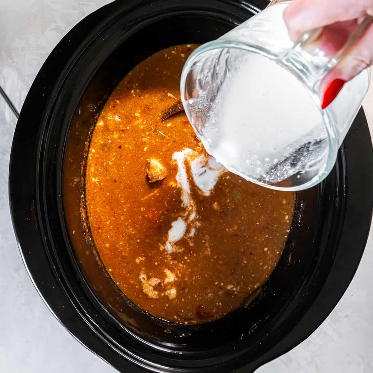 Cornstarch slurry being poured into the slow cooker over the chicken tikka masala sauce to thicken it,