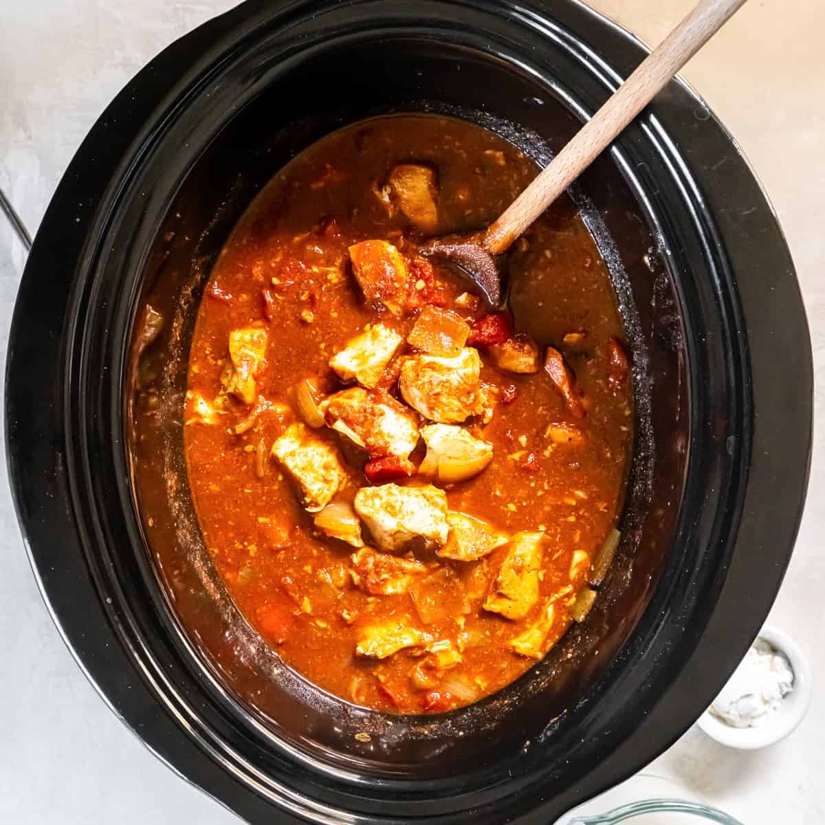 chicken tikka masala in the slow cooker after cooking, showing the thick tomato-based sauce and tender chicken before adding the coconut milk.