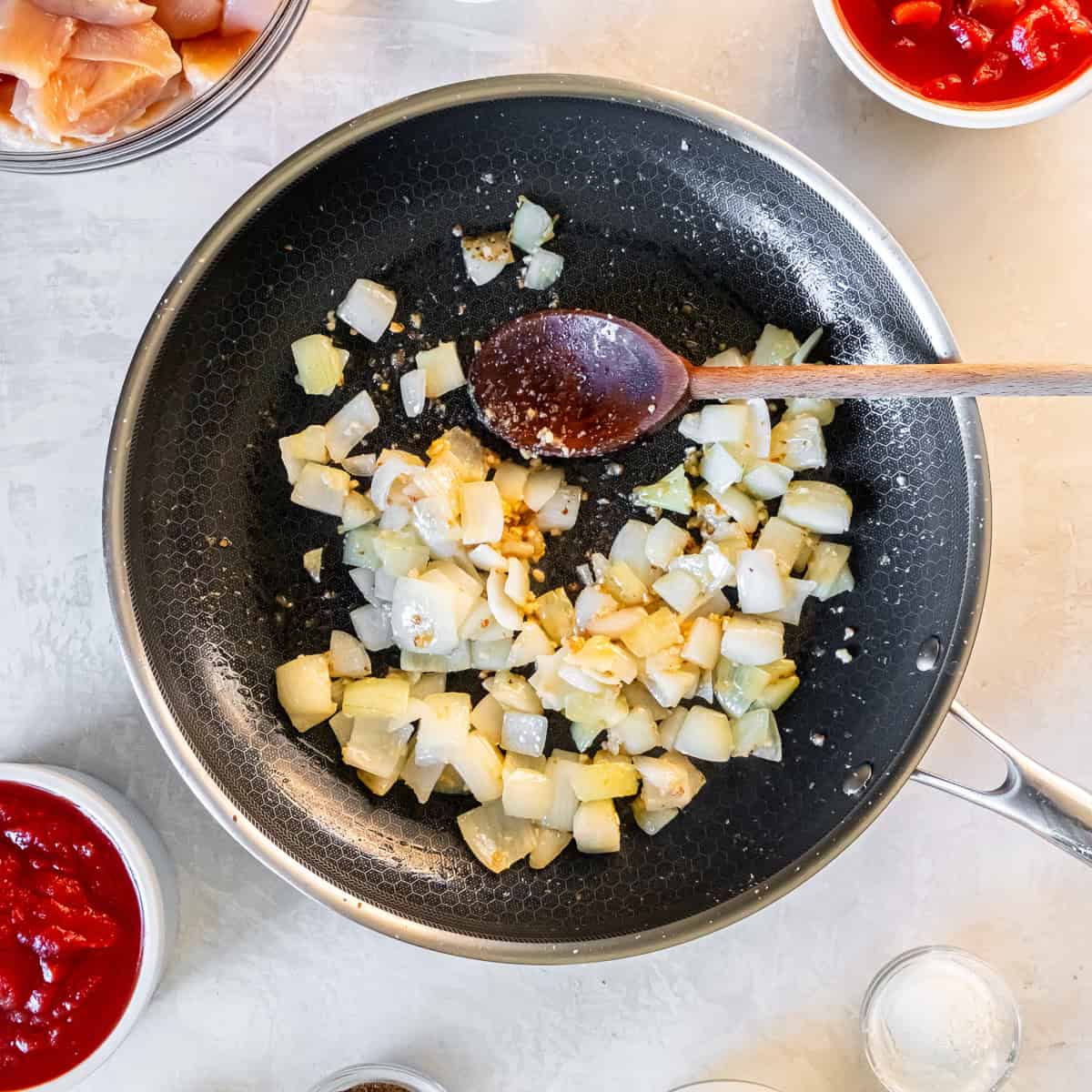 Chopped onion, garlic, and ginger sautéing in a skillet with olive oil as the base for chicken tikka masala.