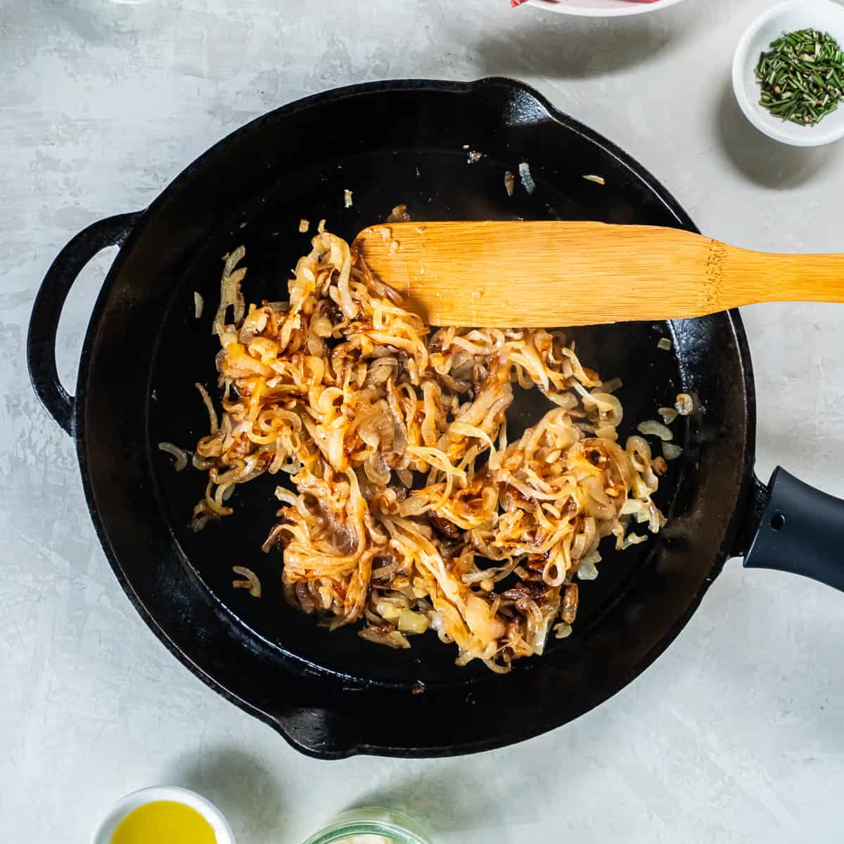 Caramelized onions cooking in a cast iron skillet with a wooden spatula, turning golden brown and tender.