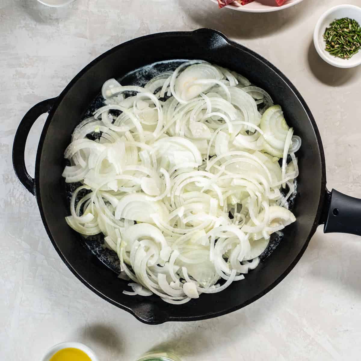 Thinly sliced onions in a cast iron skillet at the beginning of the caramelizing process.