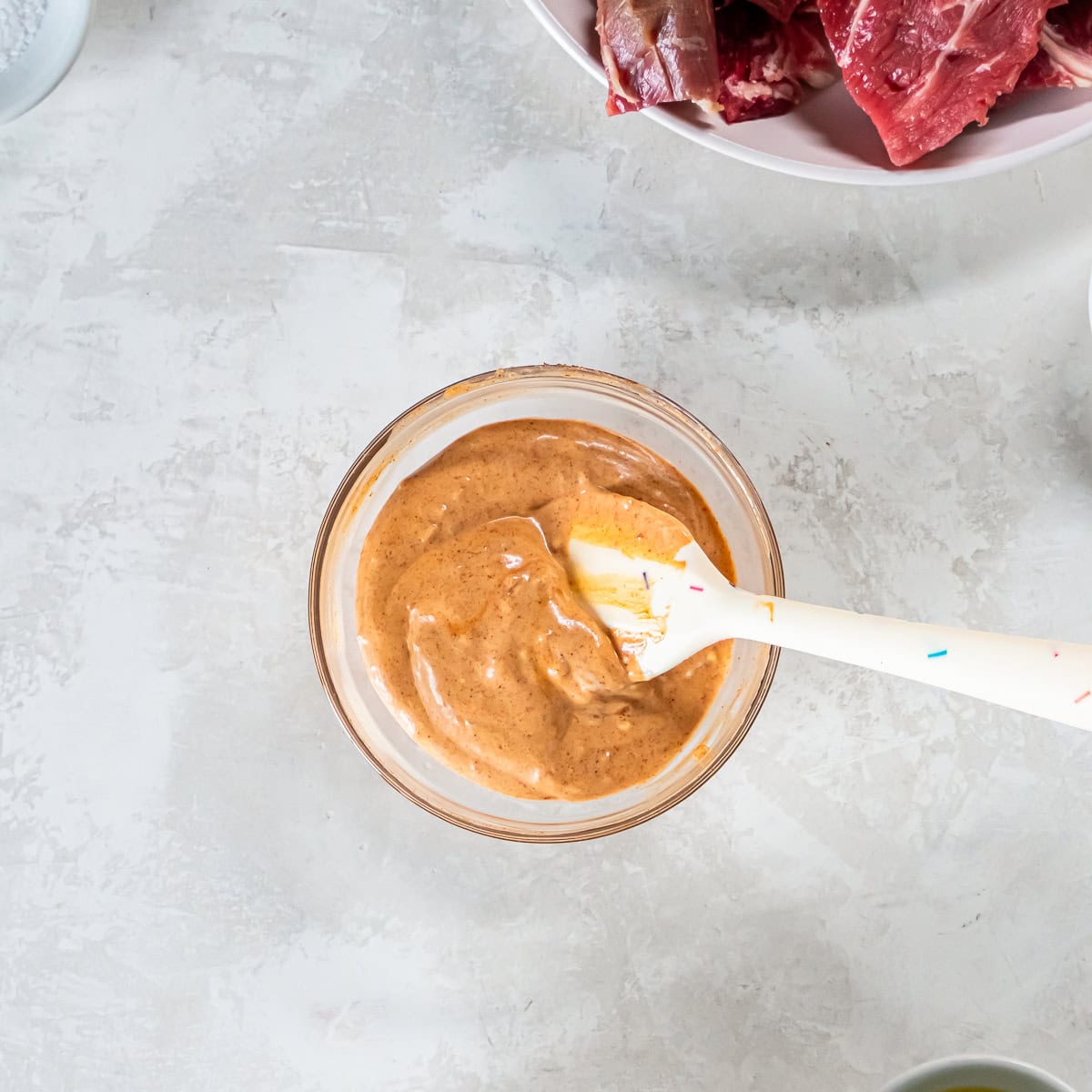 Smoky aioli sauce mixed in a small bowl with a silicone spatula, showing the creamy, light orange color.
