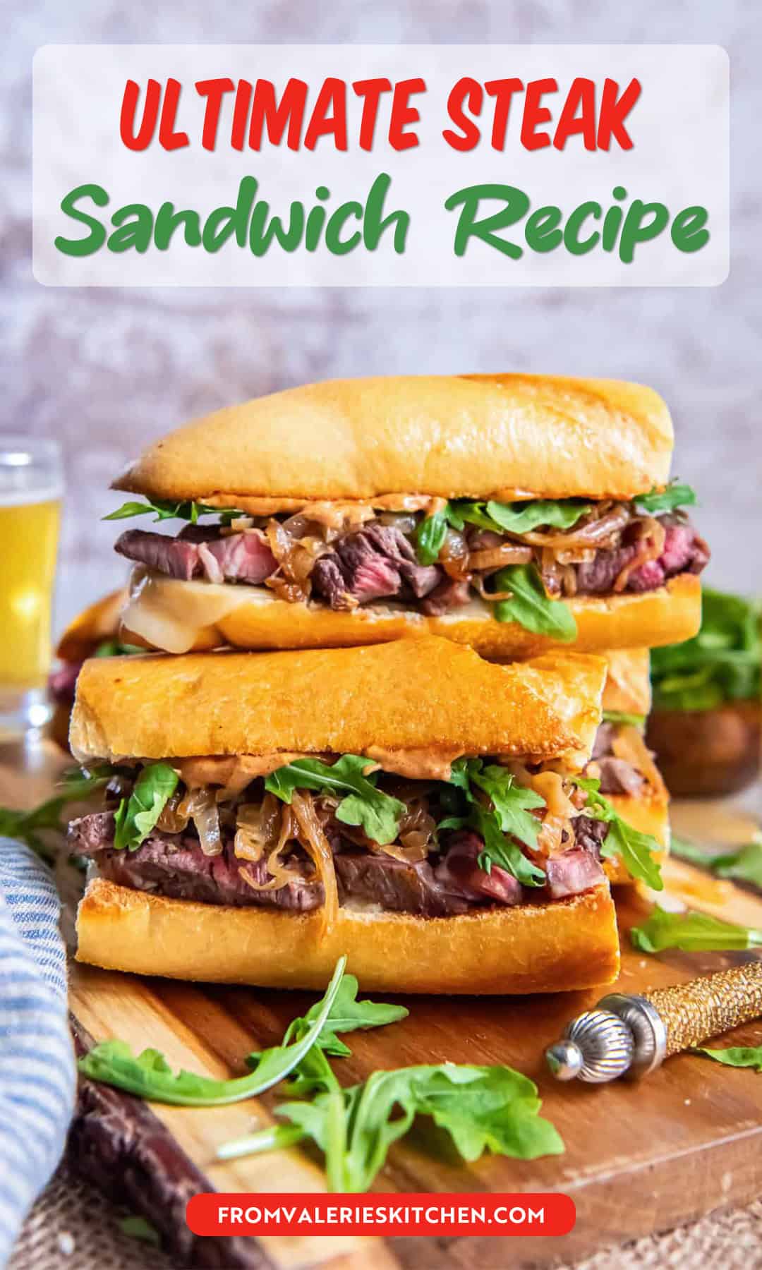 Stacked steak sandwiches with toasted baguette, sliced ribeye, melted cheese, caramelized onions, arugula, and smoky aioli on a wooden cutting board with text overlay.