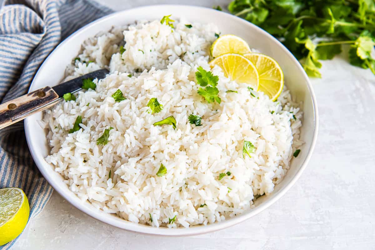 Fluffy coconut rice garnished with fresh cilantro and lime slices in a white serving bowl.