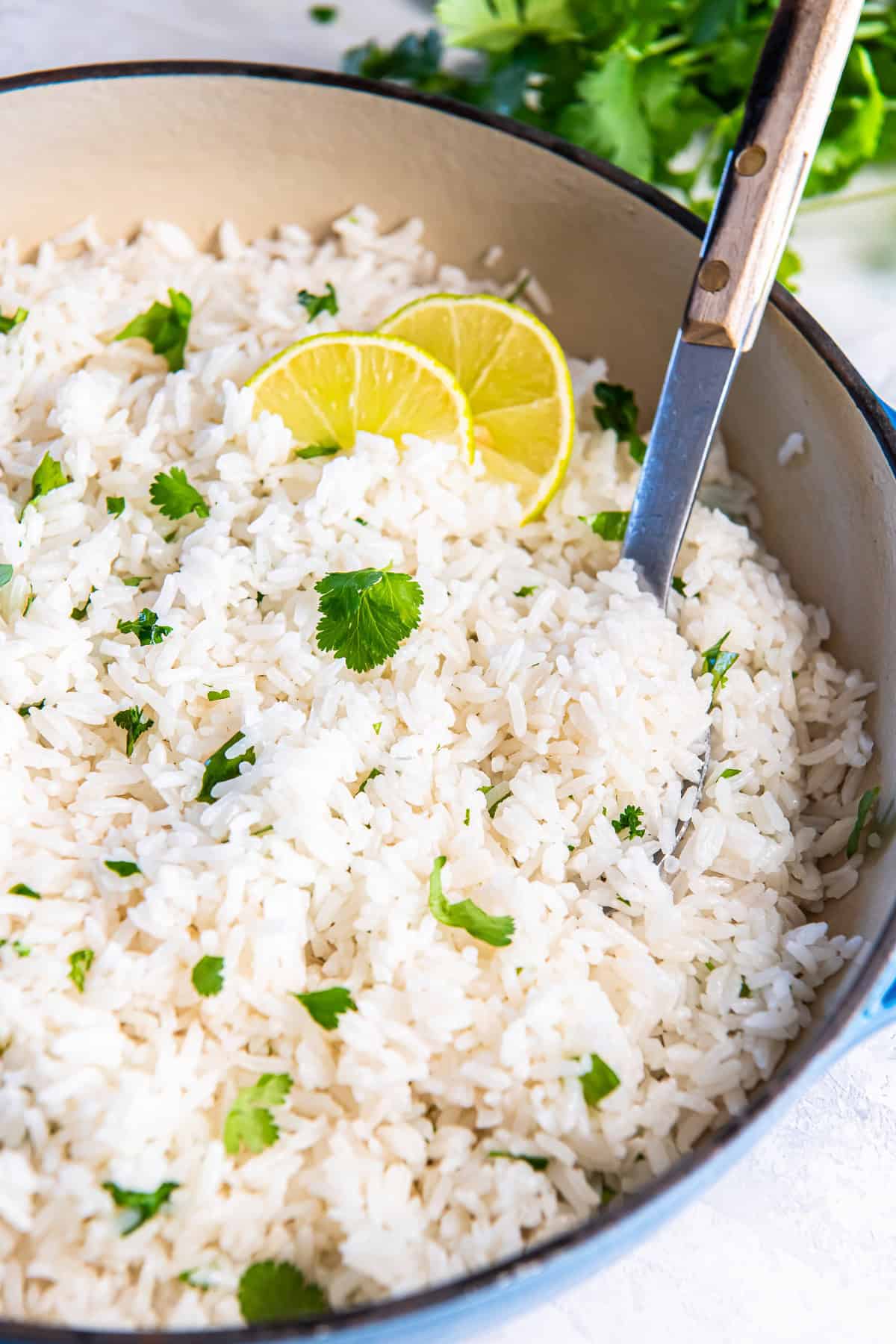 A spoon scooping coconut rice in a Dutch oven, garnished with fresh cilantro and lime.
