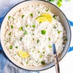 Top-down view of fluffy coconut rice with lime slices and chopped cilantro.