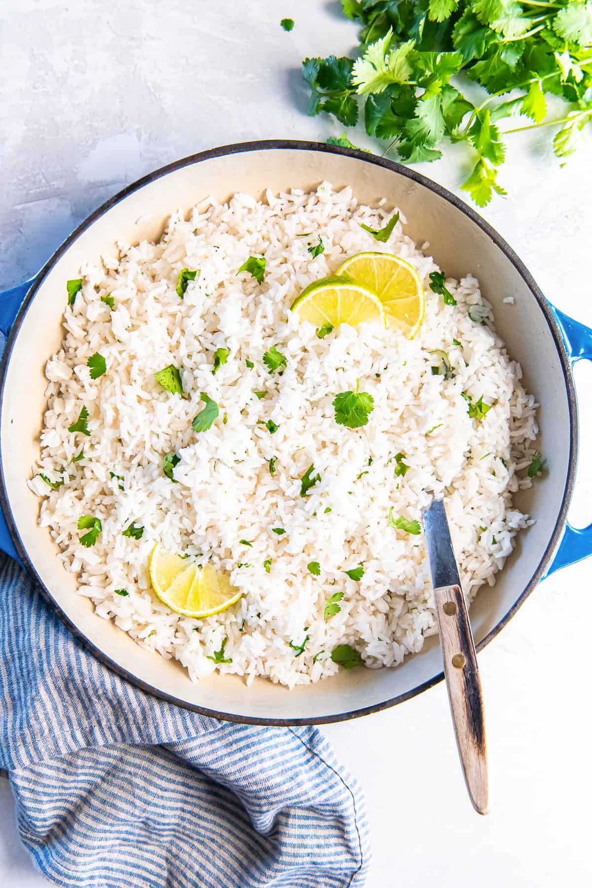 Top-down view of fluffy coconut rice with lime slices and chopped cilantro.