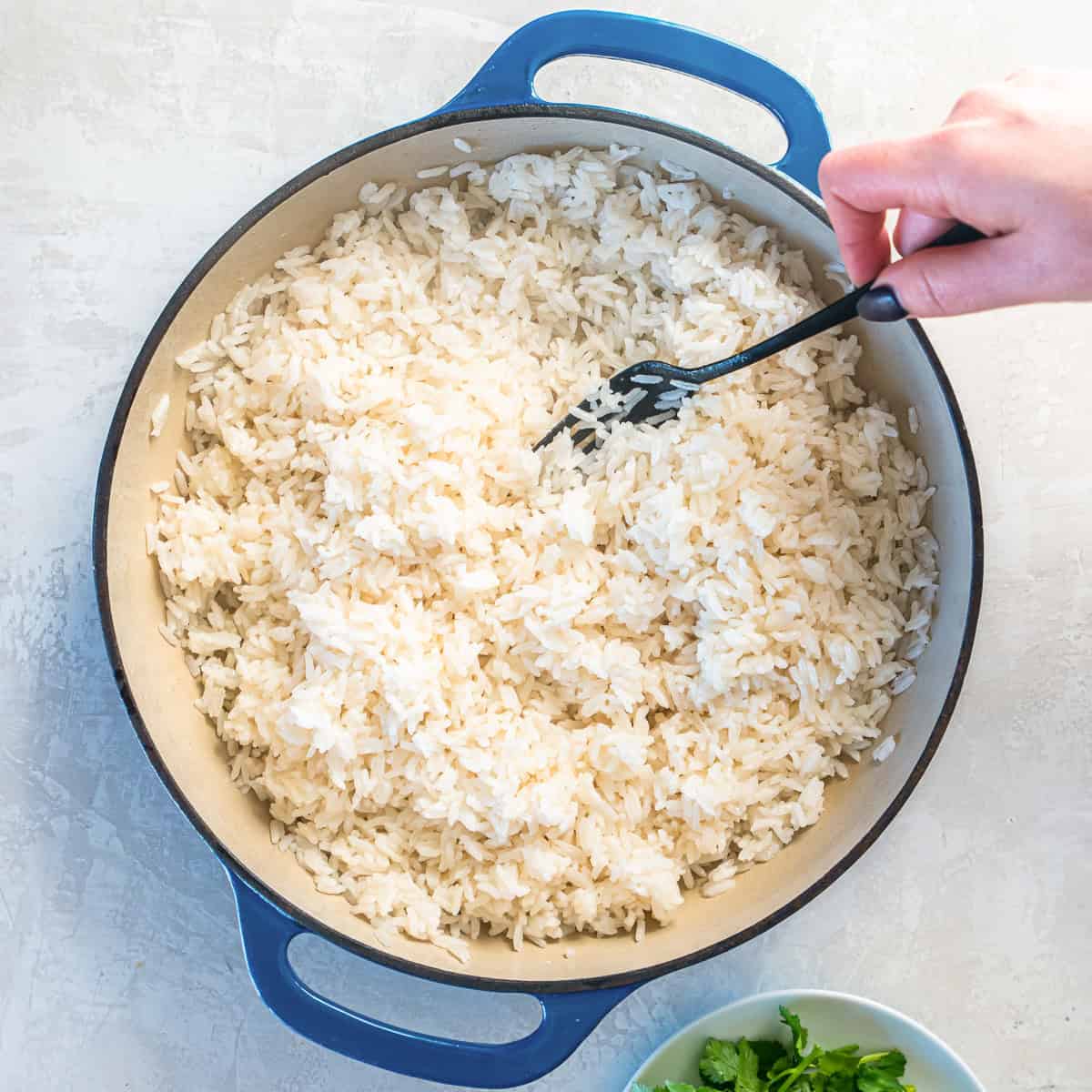 A fork fluffing coconut rice in a skillet.