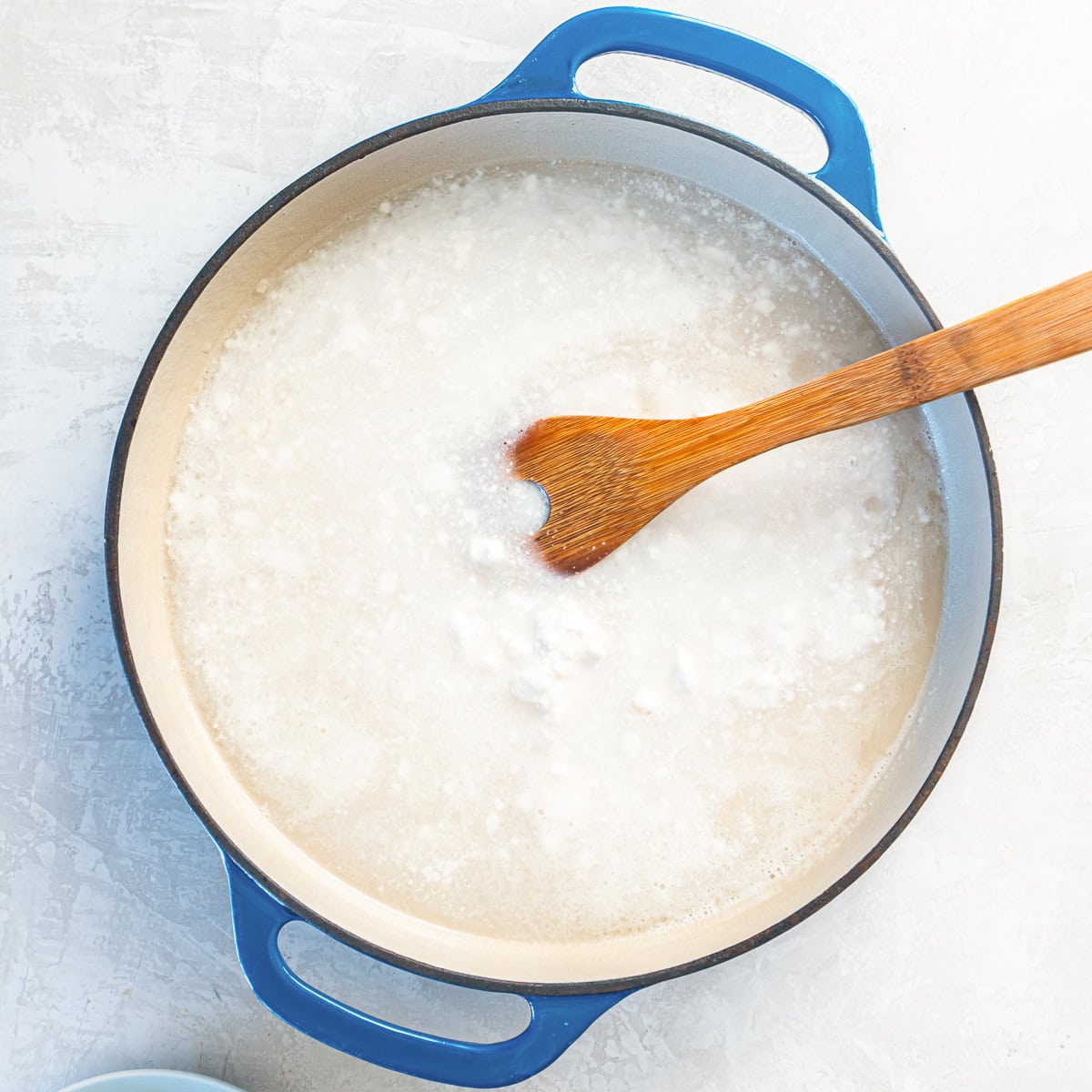 A wooden spoon stirring coconut milk into rice in a skillet.