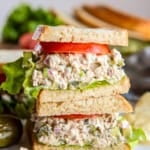 Stacked dill pickle tuna salad sandwich layered with crisp lettuce and fresh tomato on sliced bread.