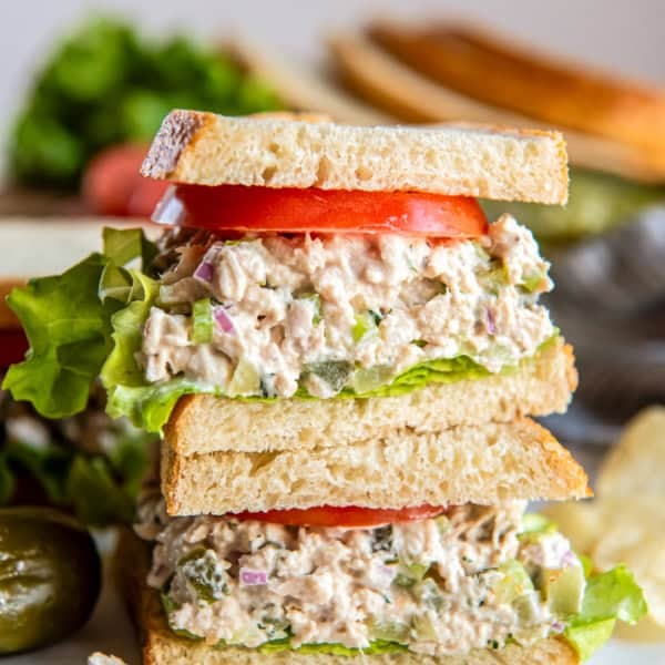 Stacked dill pickle tuna salad sandwich layered with crisp lettuce and fresh tomato on sliced bread.