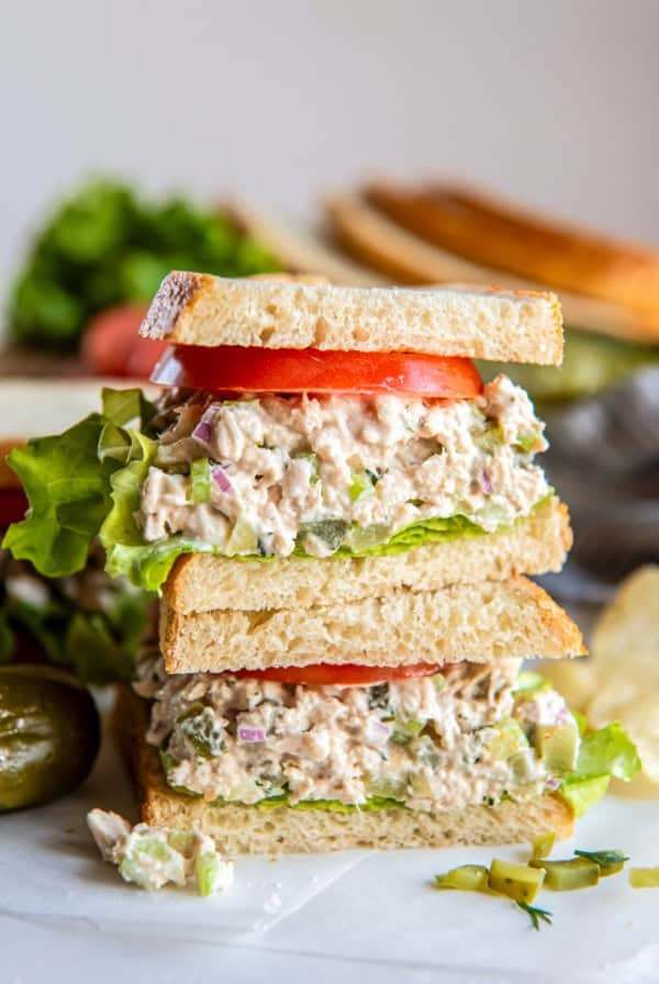 Stacked dill pickle tuna salad sandwich layered with crisp lettuce and fresh tomato on sliced bread.