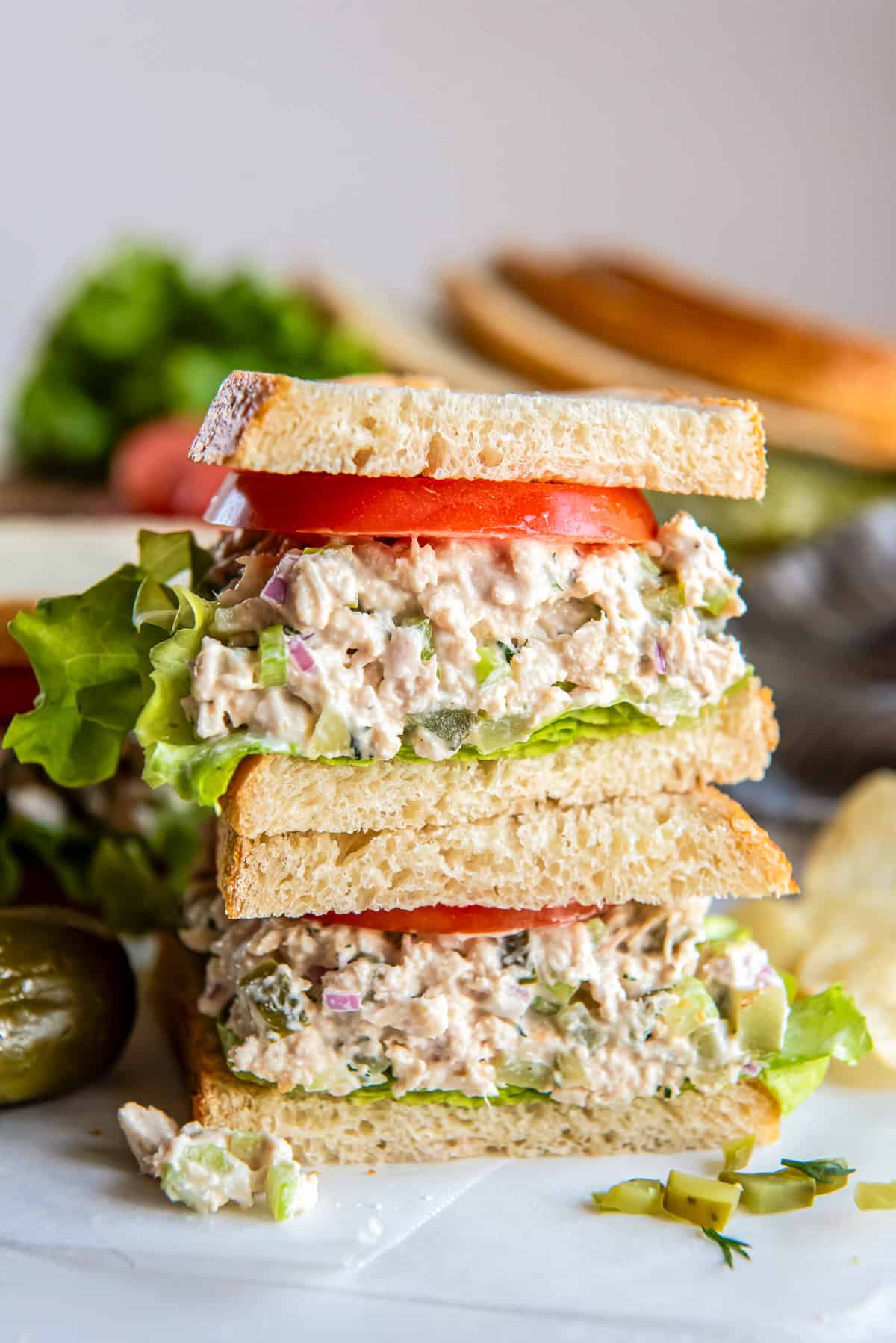 Stacked dill pickle tuna salad sandwich layered with crisp lettuce and fresh tomato on sliced bread.
