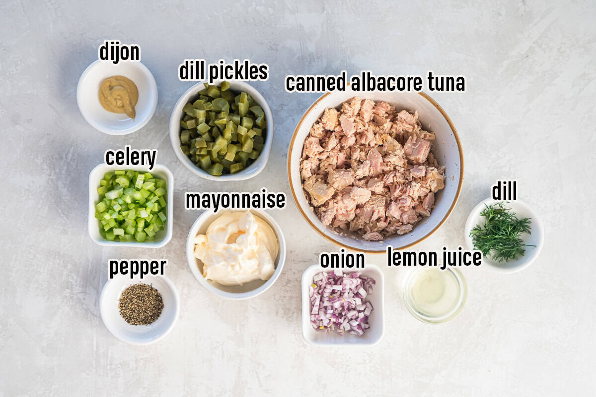 Ingredients for dill pickle tuna salad arranged in small bowls, including albacore tuna, dill pickles, mayonnaise, celery, red onion, Dijon mustard, fresh dill, lemon juice, and black pepper.