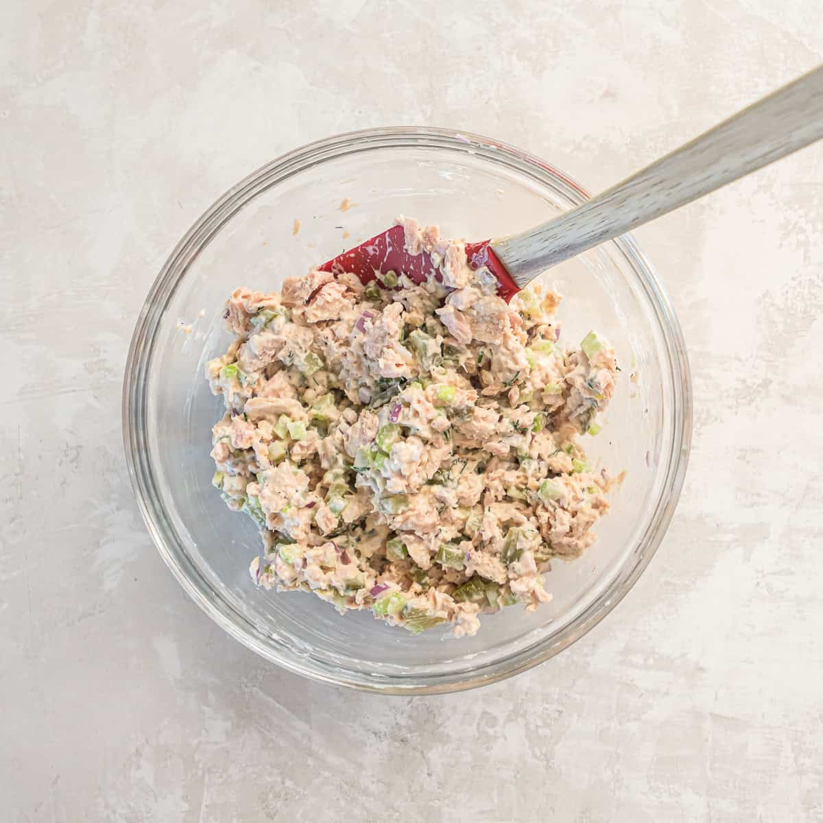 dill pickle tuna salad fully mixed in a glass bowl with a spatula.