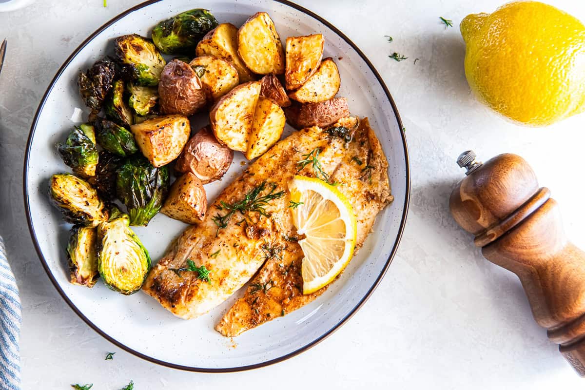 Plated easy baked fish with lemon and dill served with roasted potatoes and Brussels sprouts.
