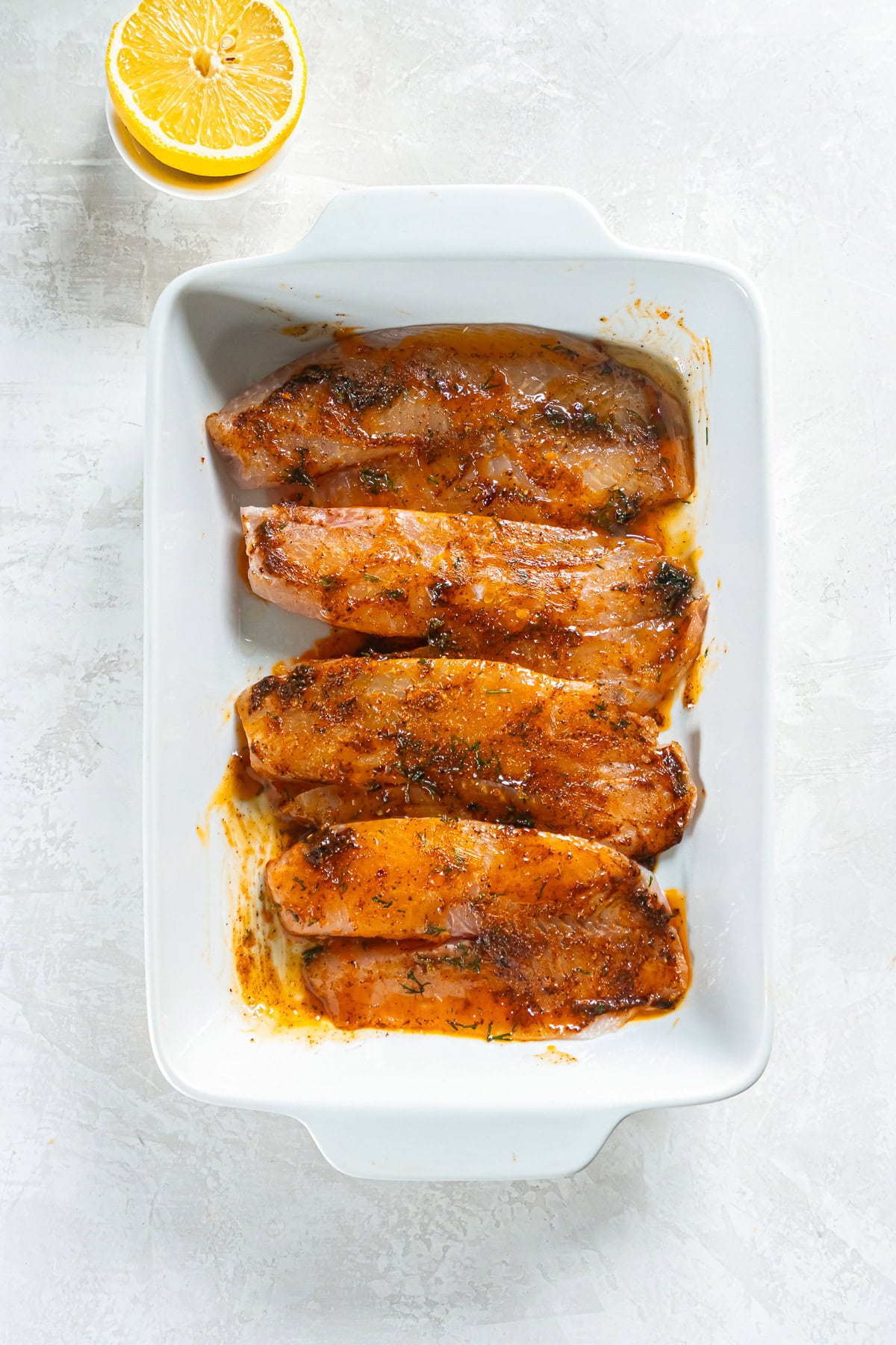 White fish fillets coated with butter, seasoning, and dill in a baking dish, ready to bake.