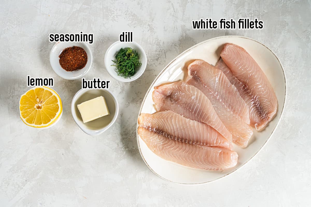 Ingredients for easy baked fish including white fish fillets, butter, lemon, fresh dill, and seasoning arranged on a light surface.