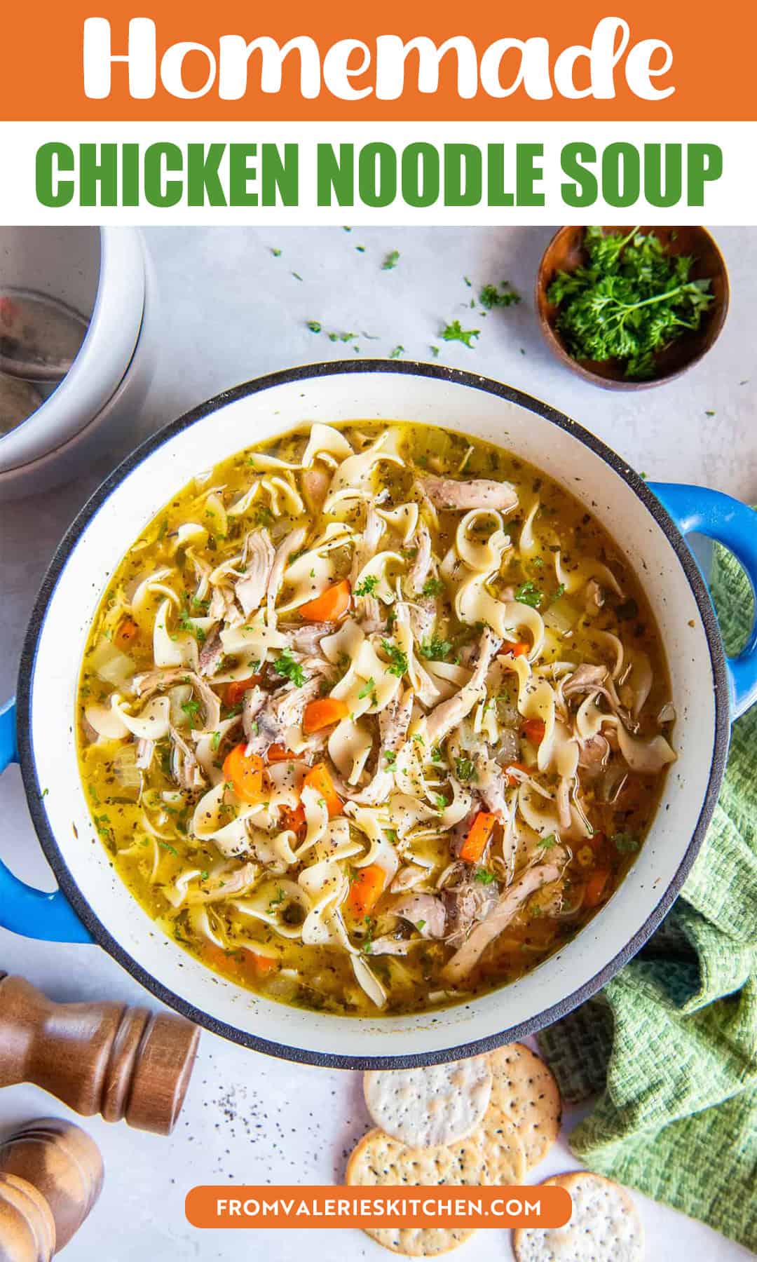 Homemade chicken noodle soup in a blue Dutch oven with egg noodles, shredded chicken, carrots, celery, and herbs, with crackers and fresh parsley nearby with text overlay.