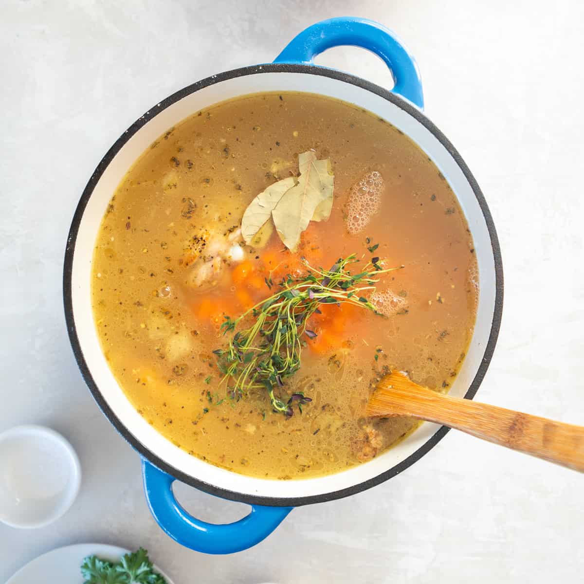 A wooden spoon stirring homemade chicken soup broth with carrots and fresh herbs.
