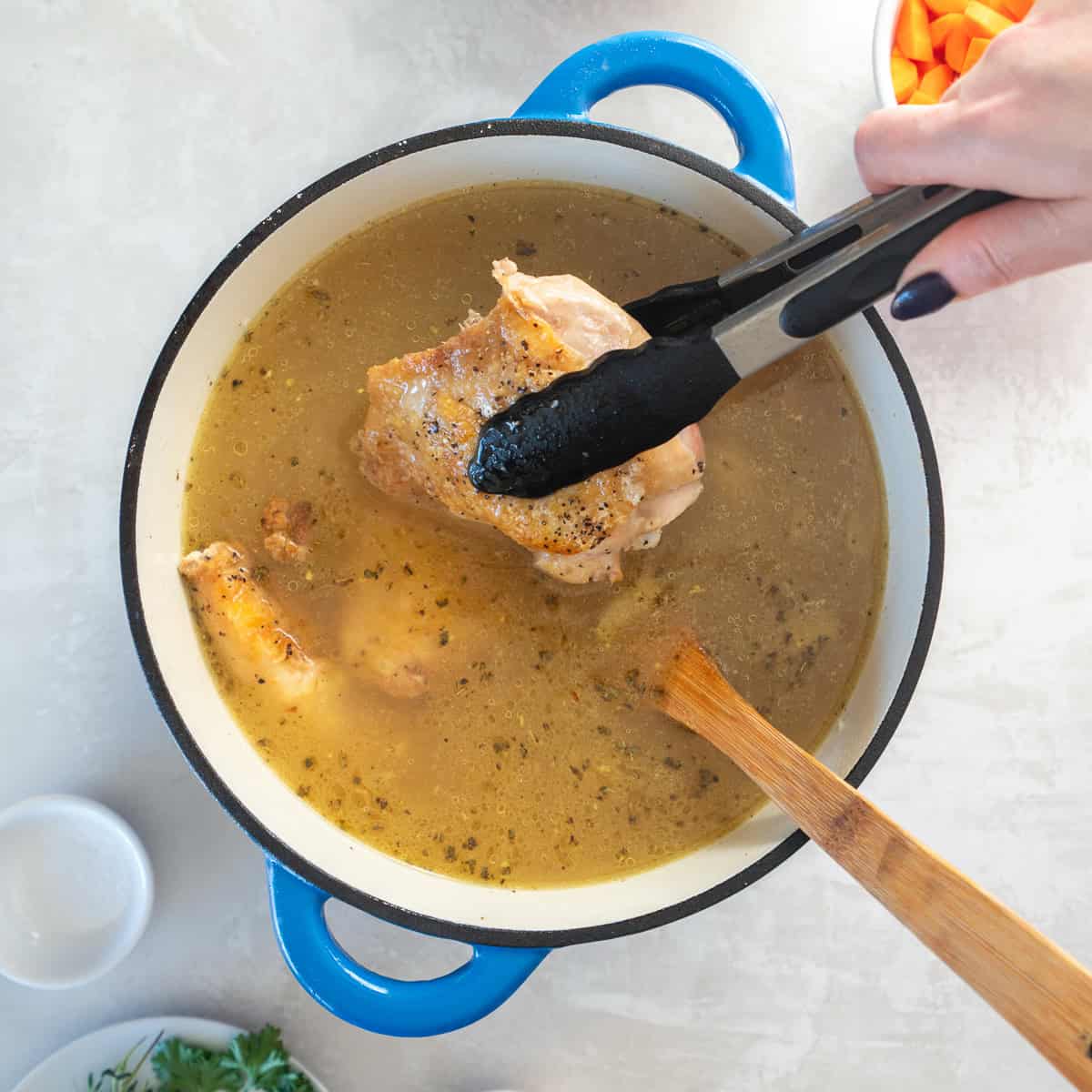 A browned chicken thigh being added to a pot of broth.