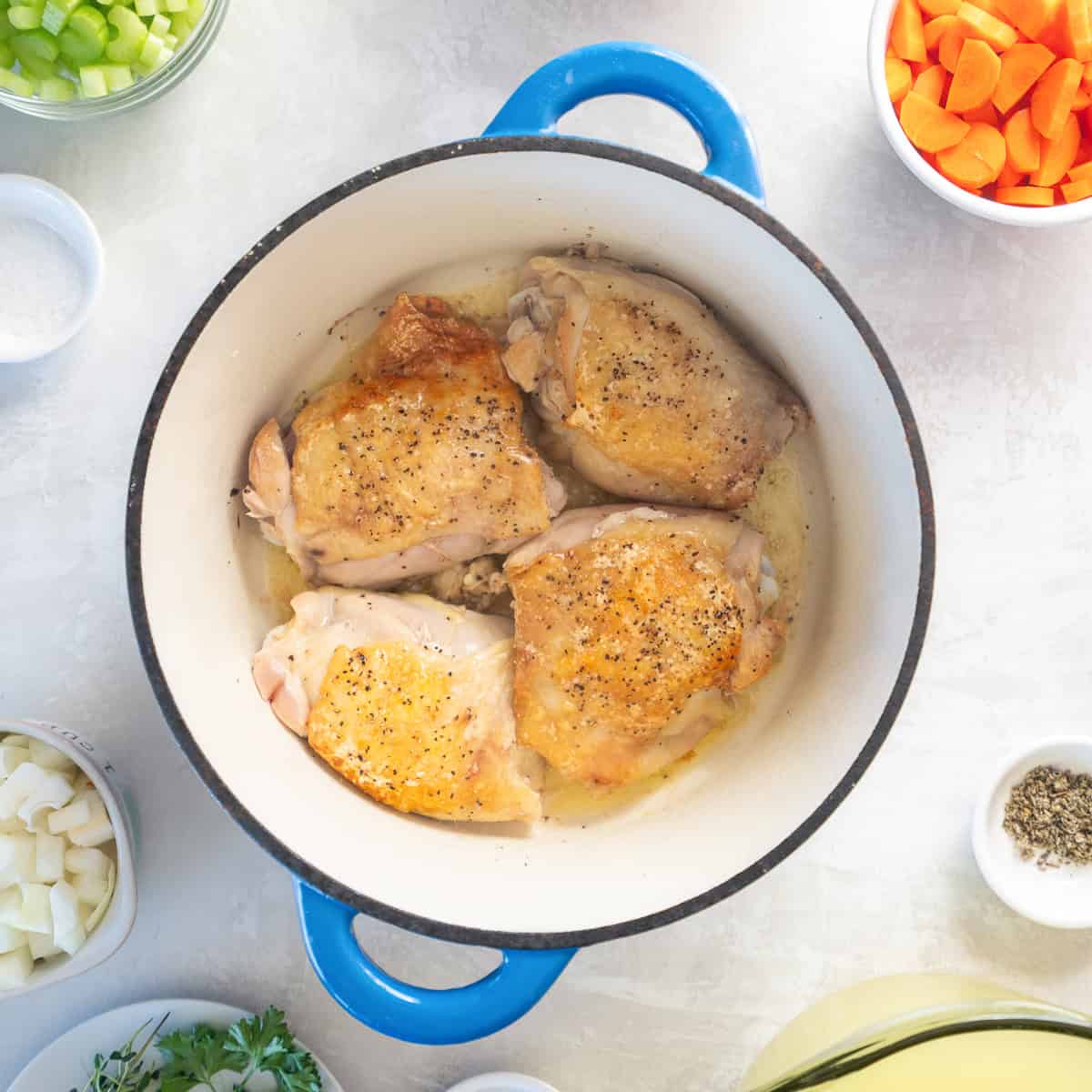 Browned skin-on chicken thighs in a blue Dutch oven.