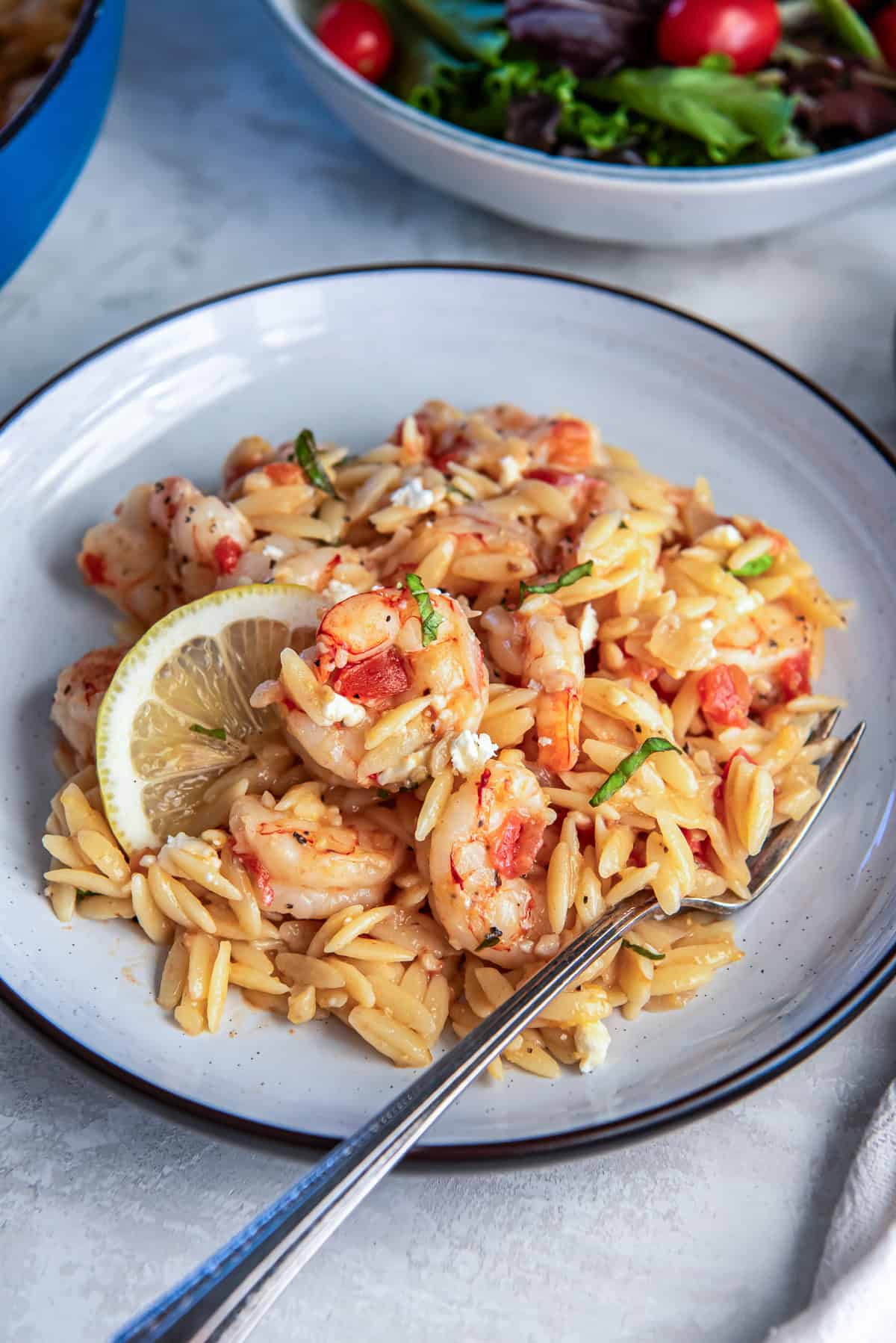 Orzo pasta with tender shrimp tomatoes feta and basil served with a lemon wedge.