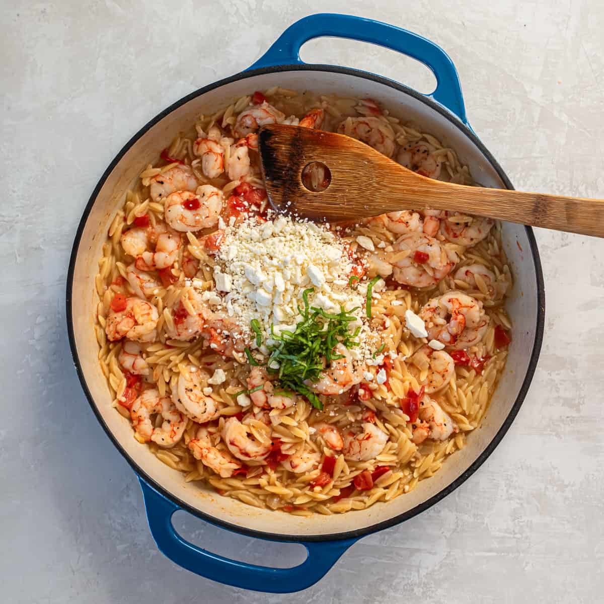 Crumbled feta cheese and fresh basil added to shrimp orzo in the skillet.