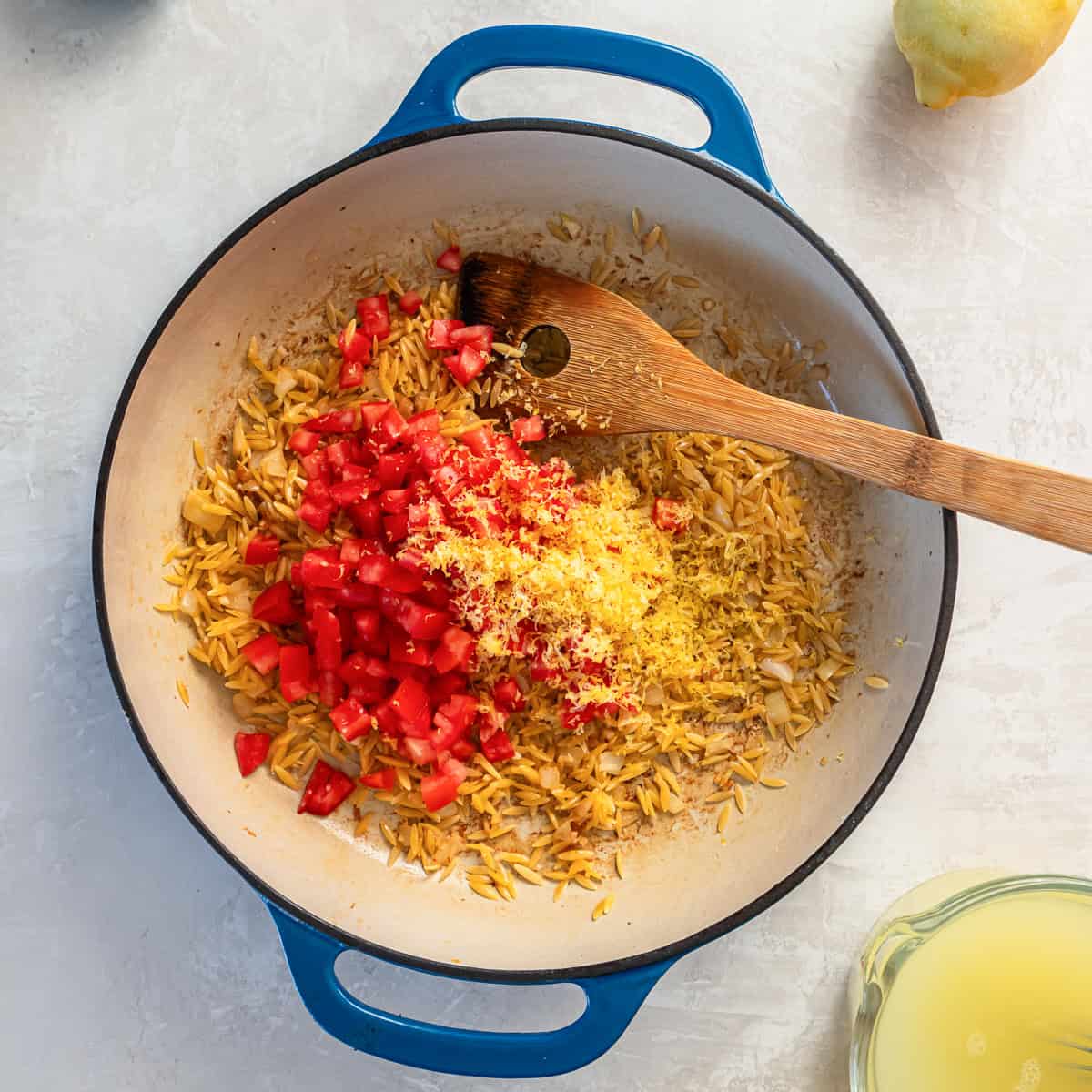 Diced tomatoes and lemon zest added to toasted orzo in a skillet.