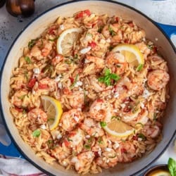 Orzo pasta with shrimp, feta, and tomatoes in a skillet with lemon slices.