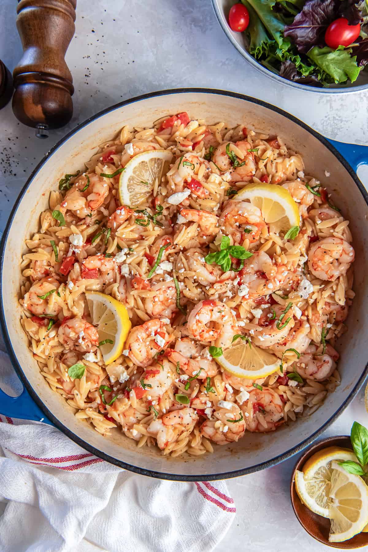Orzo pasta with shrimp, feta, and tomatoes in a skillet with lemon slices.