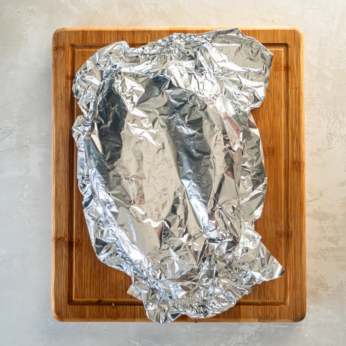 Oven roasted pork tenderloin covered on a cutting board tented with foil.