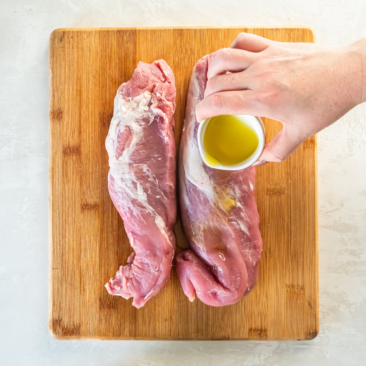 Oil being poured over pork tenderloin.