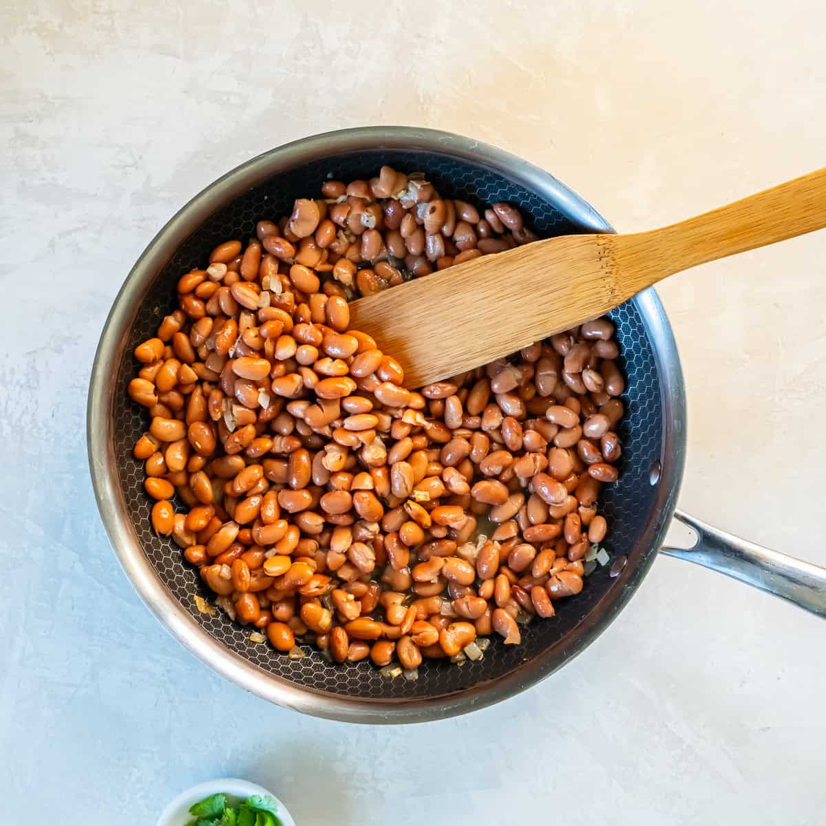 Seasoned pinto beans stirred in a skillet as they heat through